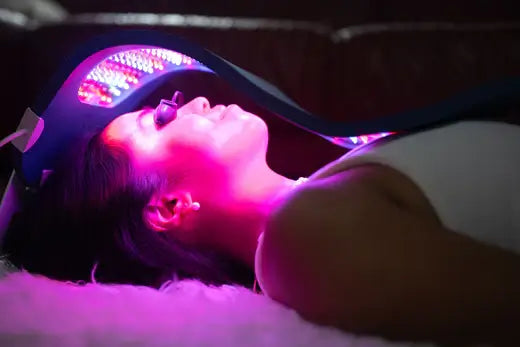 Woman laying on a bed receiving LED red light therapy treatment on her face with a Celluma Pro device