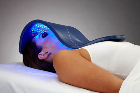 Woman lying down with a Celluma PRO PLUS LED light therapy panel positioned over her face