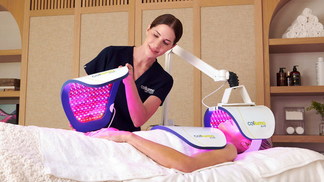 Esthetician placing a panel onto a clients hands while they lie on a massage table with additional panels over their neck/chest and face from the Celluma ELITE device
