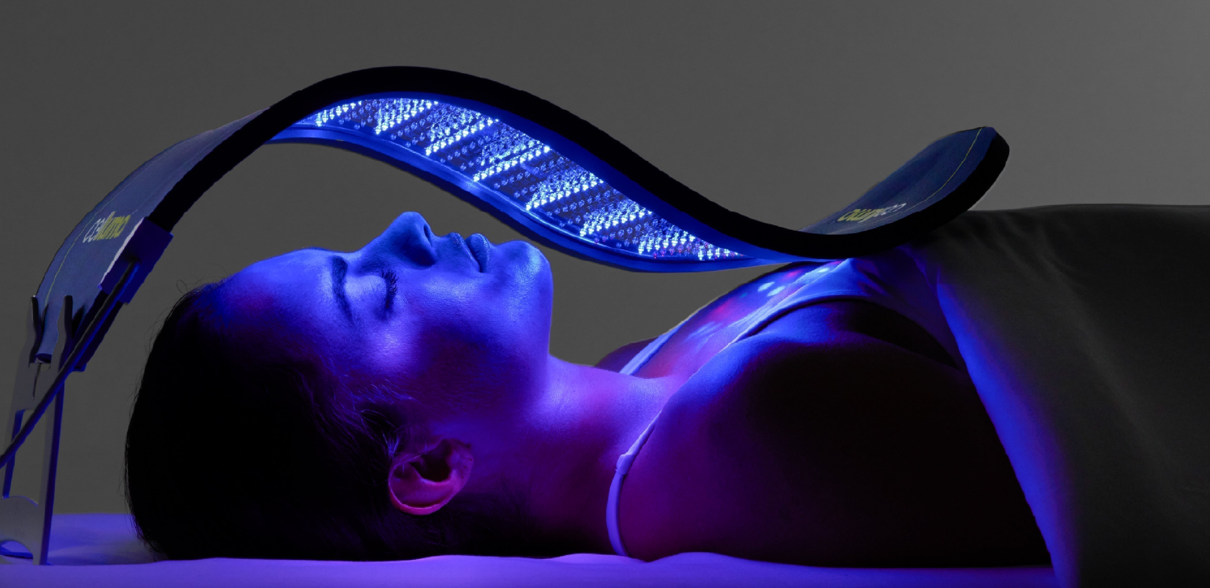 Woman using a large Celluma LED light therapy panel in blue light mode to treat acne and skin