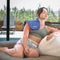 Women sitting on her couch at home using the Celluma HOME LED light therapy device to treat aches and pains in her shoulder.